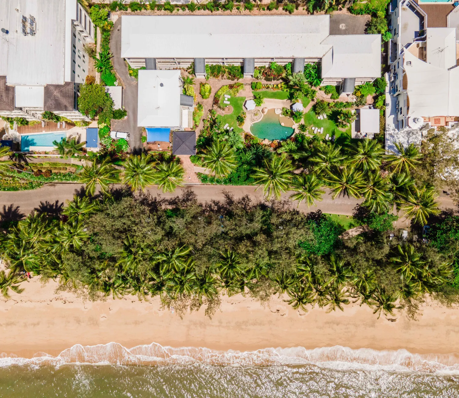 birds eye view of Melaleuca Resort Showing the pool and outdoor area with lush gardens with a line of palms trees separating it from the beach.