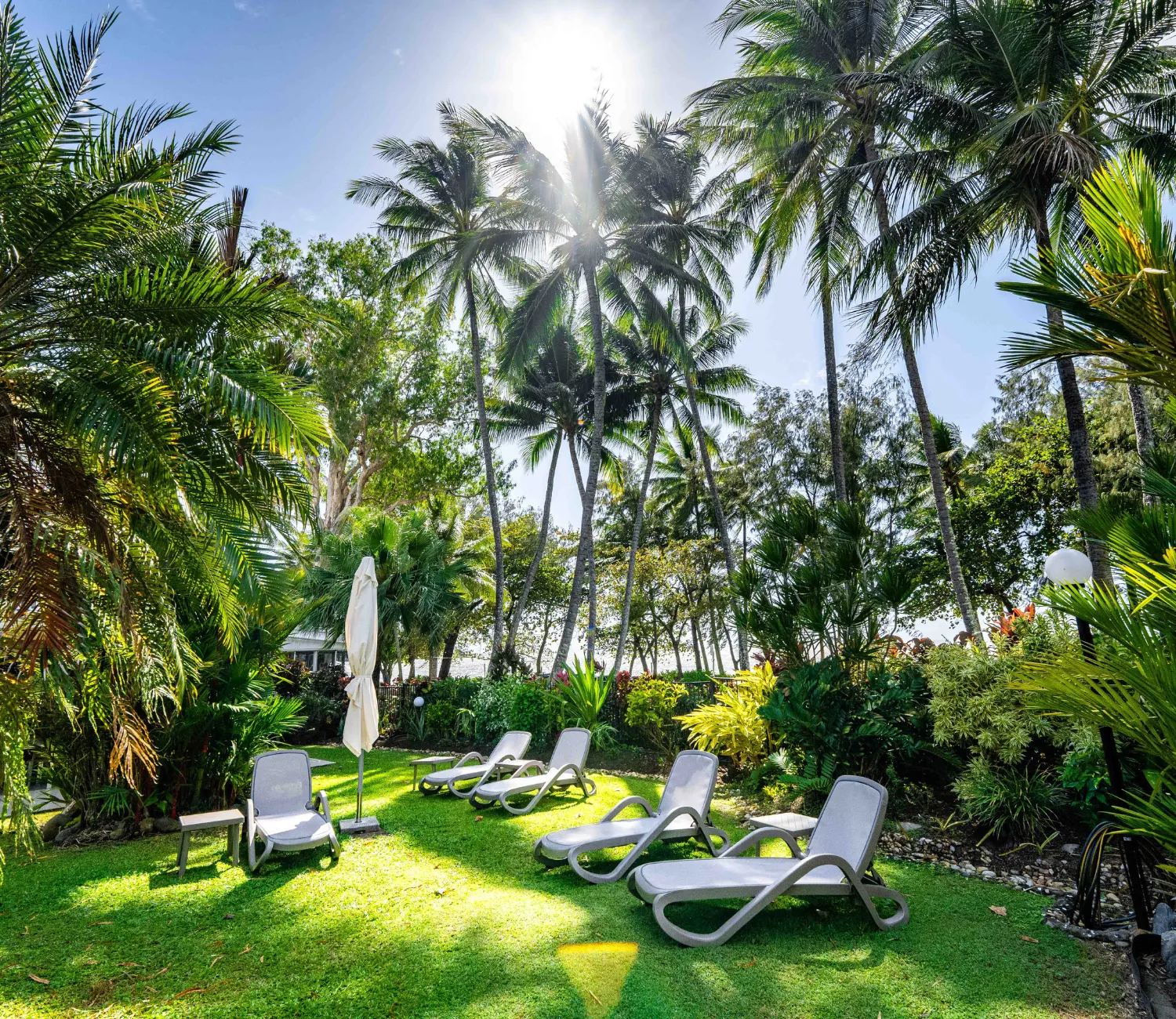 Grass area near pool with sun chairs and umbrellas surrounded by garden
